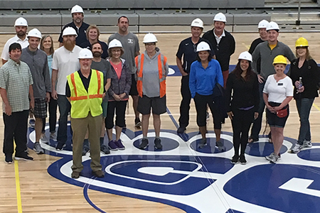 Group picture of coaches on the court with hard hats on.